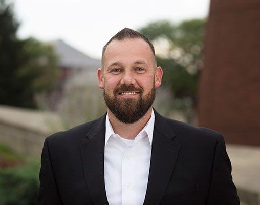 A man with a beard is wearing a black suit and white shirt.