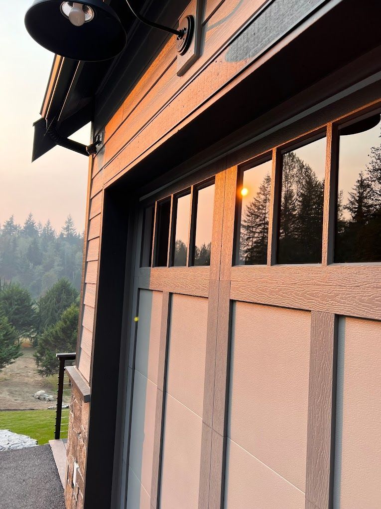 Garage exterior with reflected sunset, gray door, light, and forest backdrop.