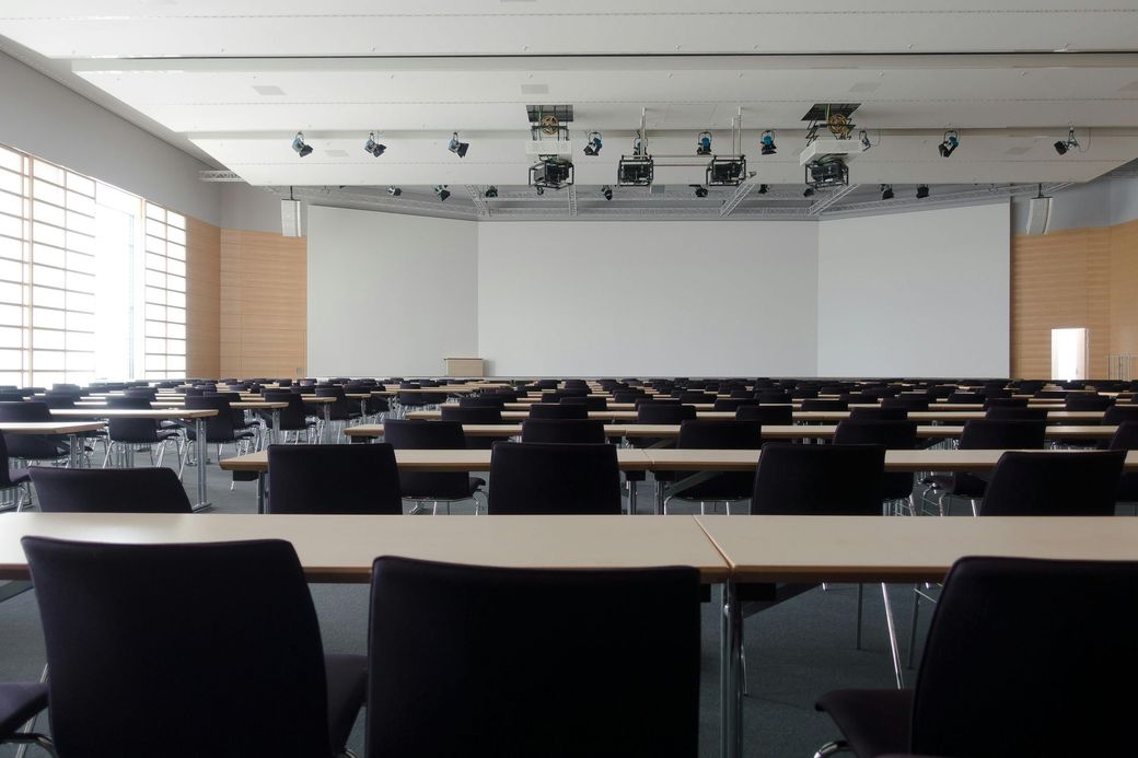 An empty conference room with tables and chairs and a large screen.