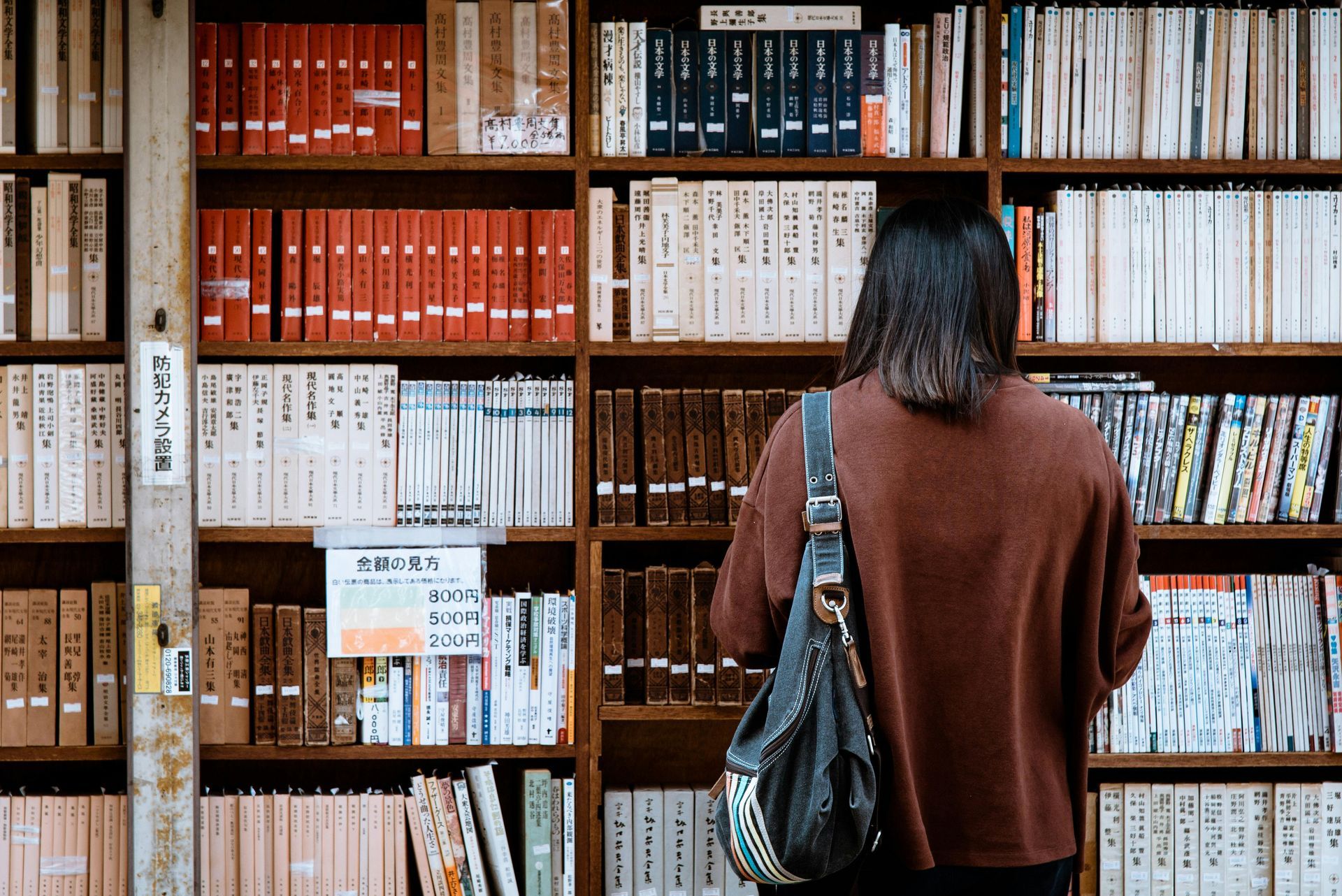 A woman is looking at books on a bookshelf in a library.