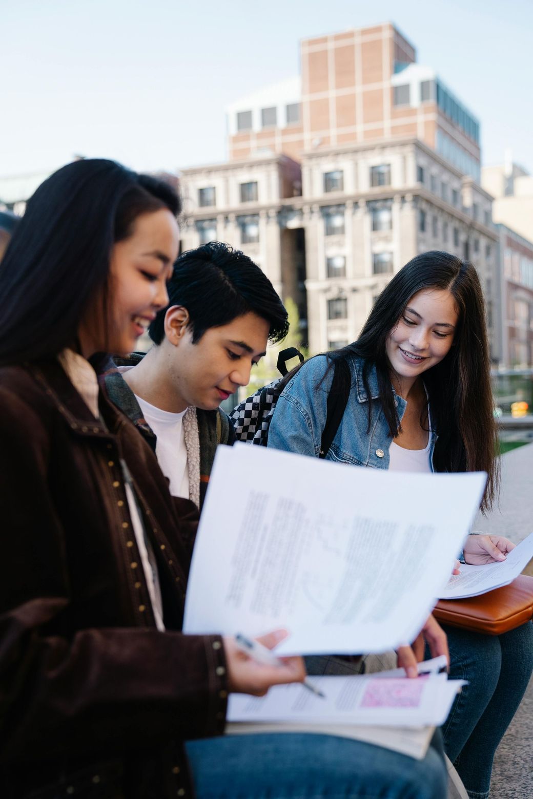 A group of young people are sitting on a bench looking at papers.