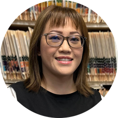 A woman wearing glasses is smiling in front of a shelf of medical records.