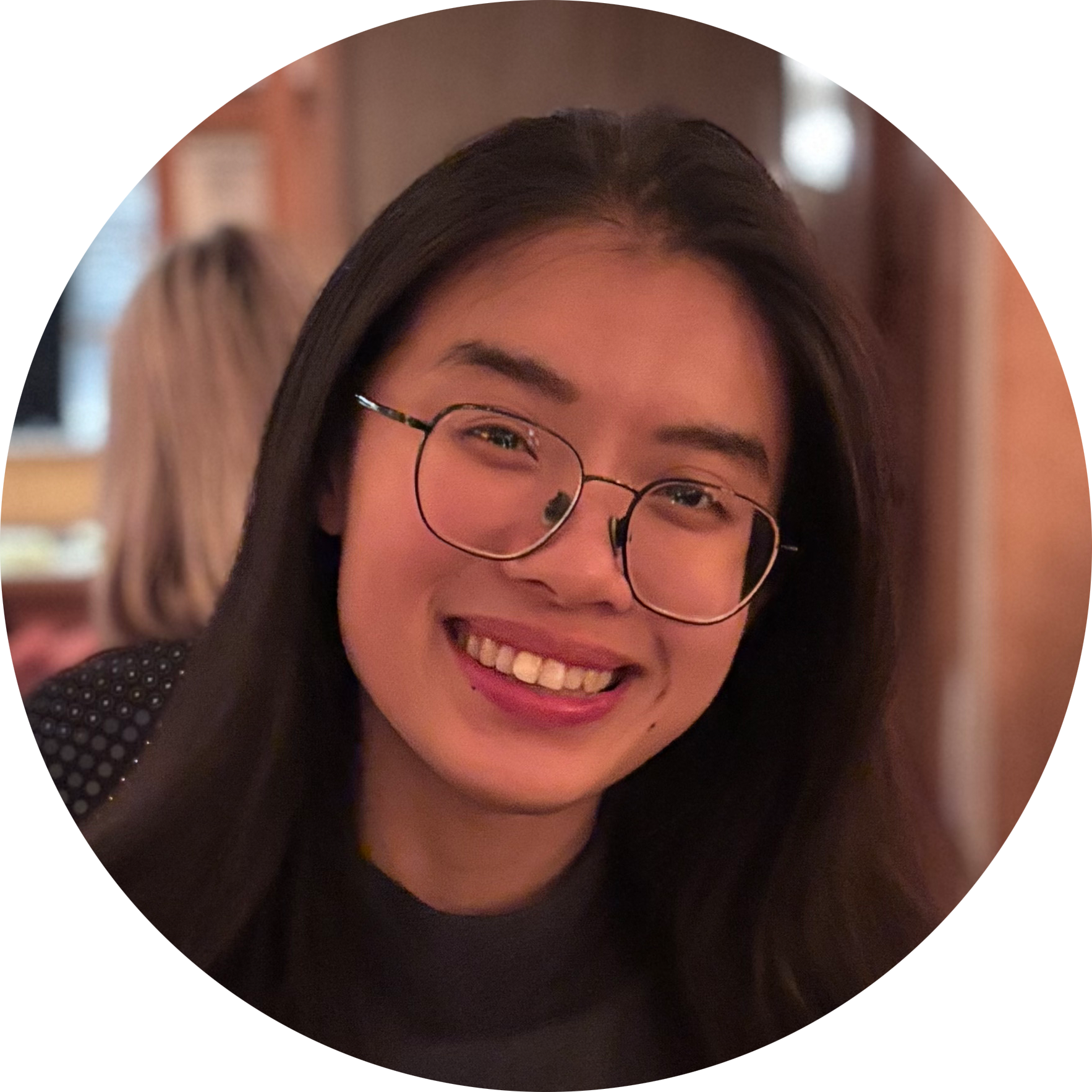 A woman with long hair is smiling in a circle with trees in the background.