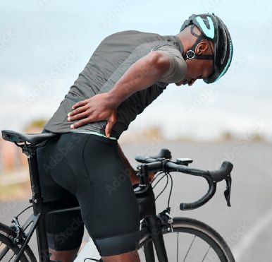 A man wearing a helmet is holding his back while riding a bike