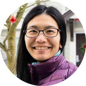 A woman with long hair is smiling in a circle with trees in the background.