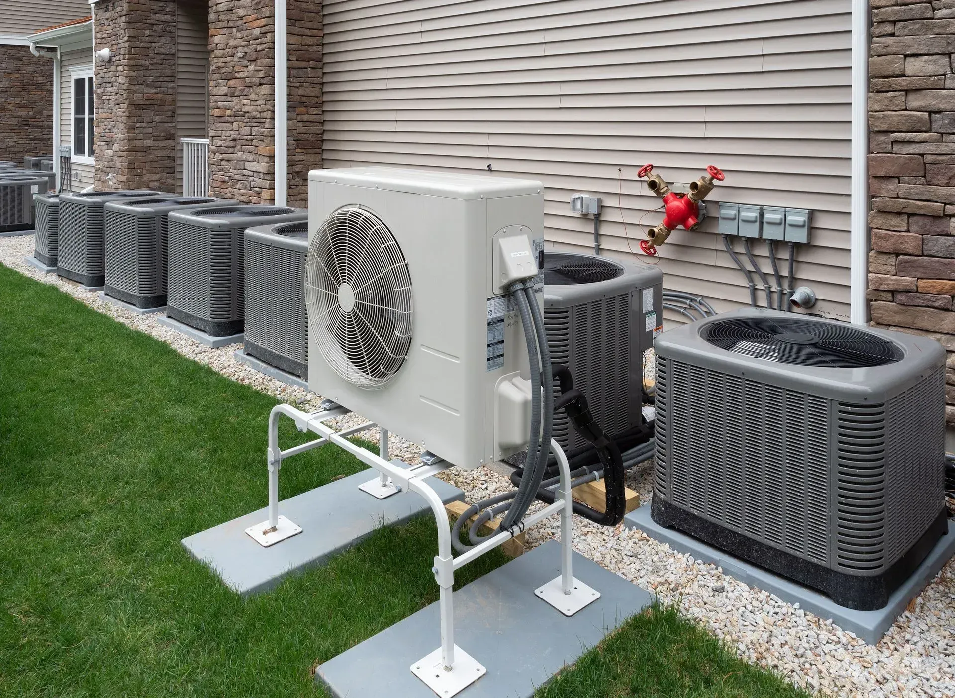 Outdoor air conditioning units lined up on grass next to a building.