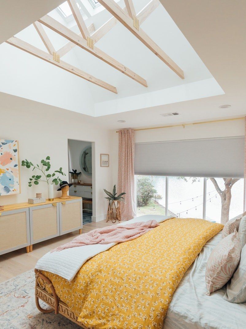 Bright bedroom with skylight, yellow bedding, cream dresser, and pink curtains.