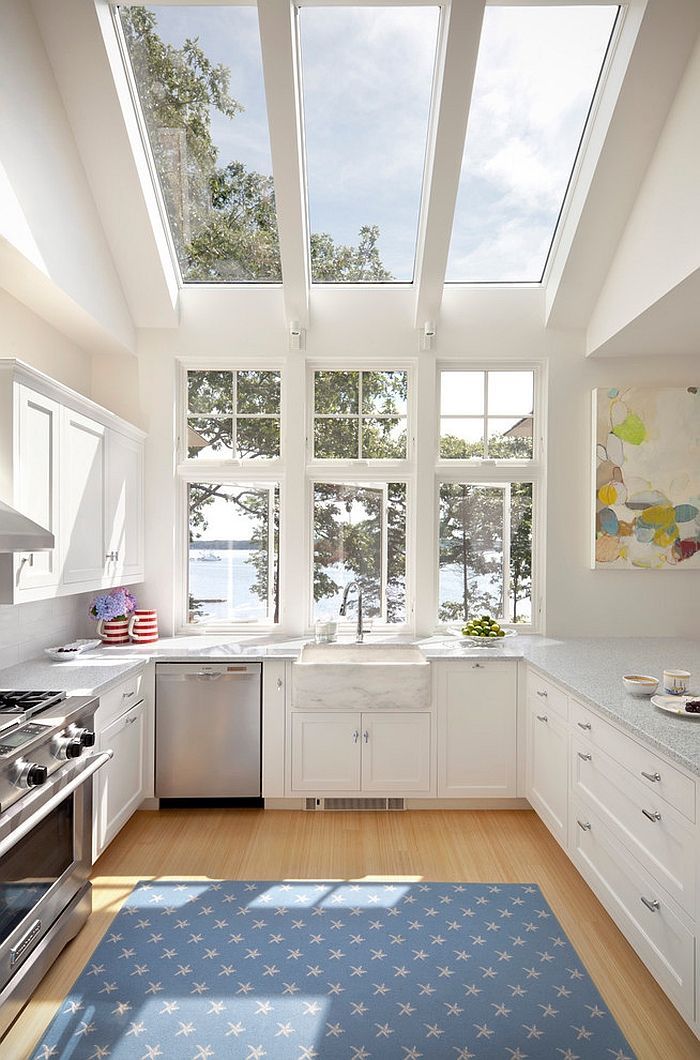 White kitchen with skylights, windows overlooking water, stainless steel appliances, and blue rug.