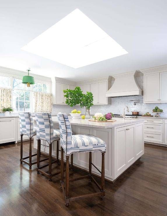 Bright white kitchen with island, seating, and a skylight. Wooden floors and white cabinets.