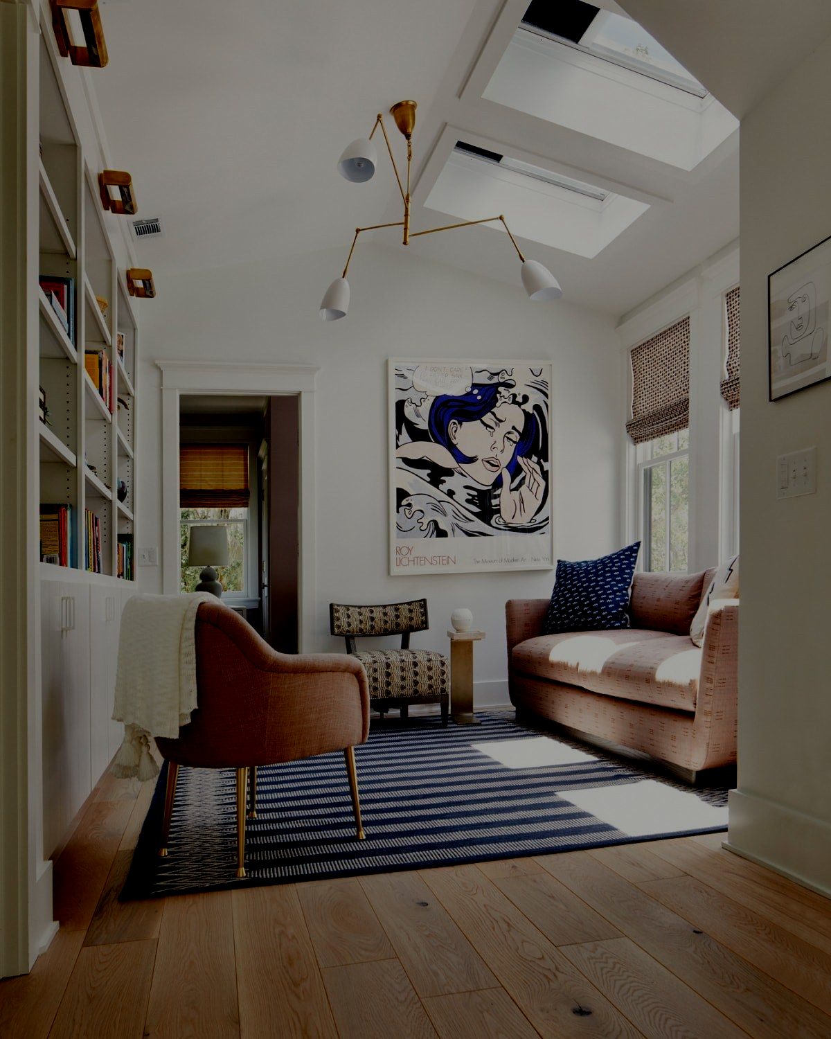 Cozy room with blue rug, pink sofa, art print, and built-in bookshelf. Skylights provide natural light.