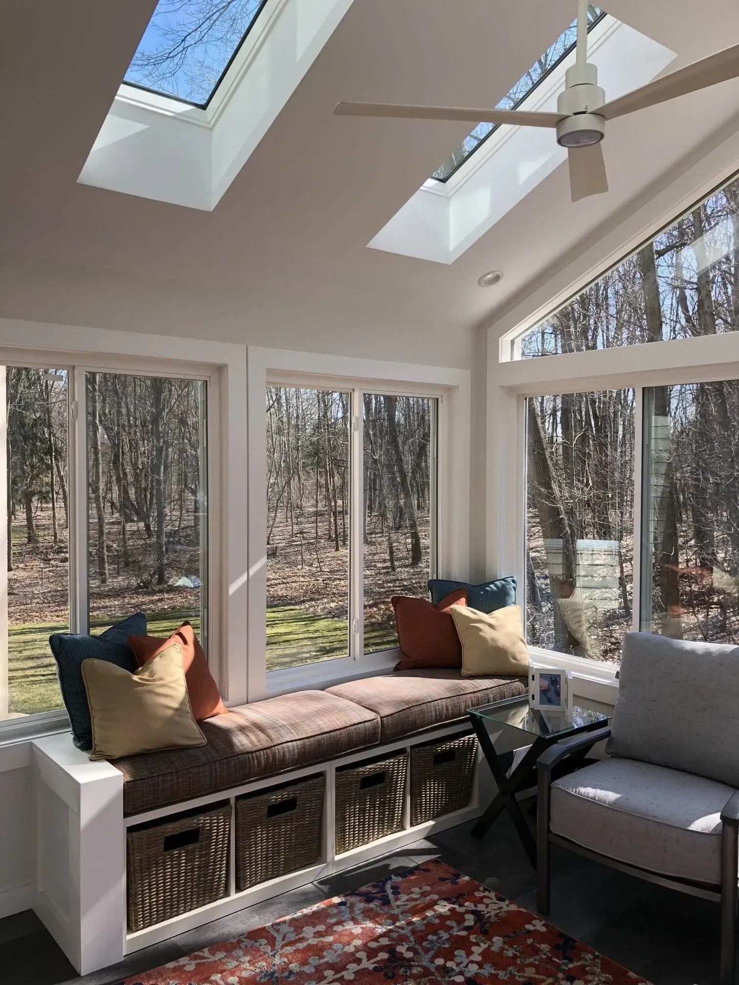 Sunroom with large windows, skylights, built-in bench with pillows, wicker baskets, and a rug.