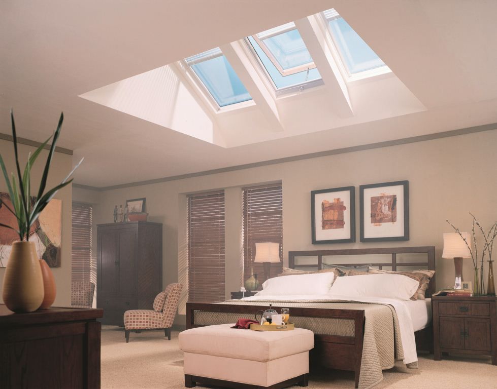 Bedroom with skylights, featuring a bed, nightstands, artwork, and a vase with branches.