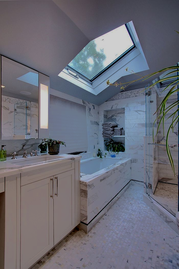 Modern bathroom with skylight, white marble, tub, shower, and vanity.
