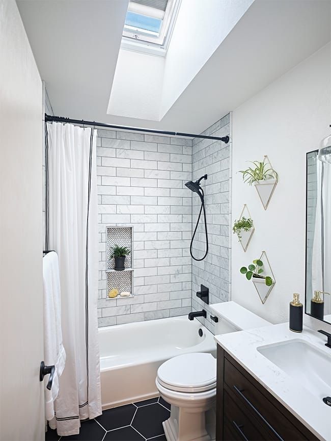 Small white bathroom with black accents: subway tile shower, hexagon floor, skylight.