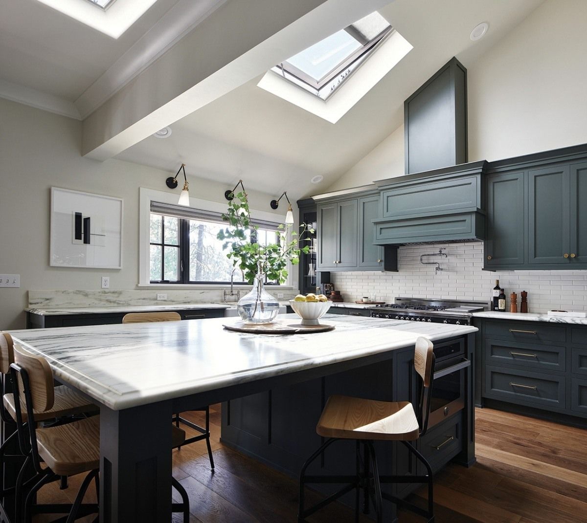 Kitchen with marble island, dark green cabinets, skylight, and wooden floors.