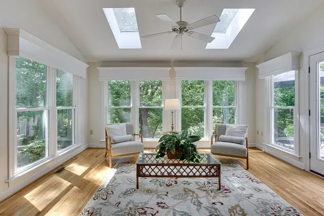 Sunroom with windows, two chairs, a coffee table, and a ceiling fan. Natural light fills the room with a rug on the floor.