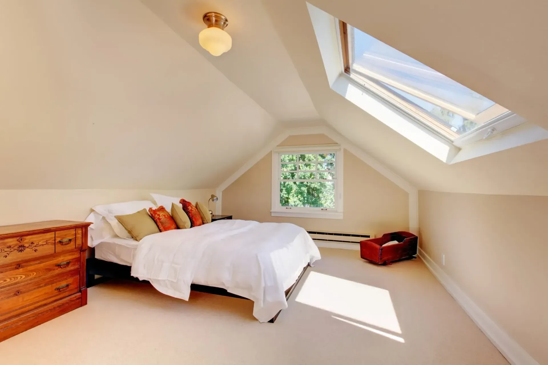 Bedroom with white bedding, skylight, and wooden dresser. Beige walls and carpet.
