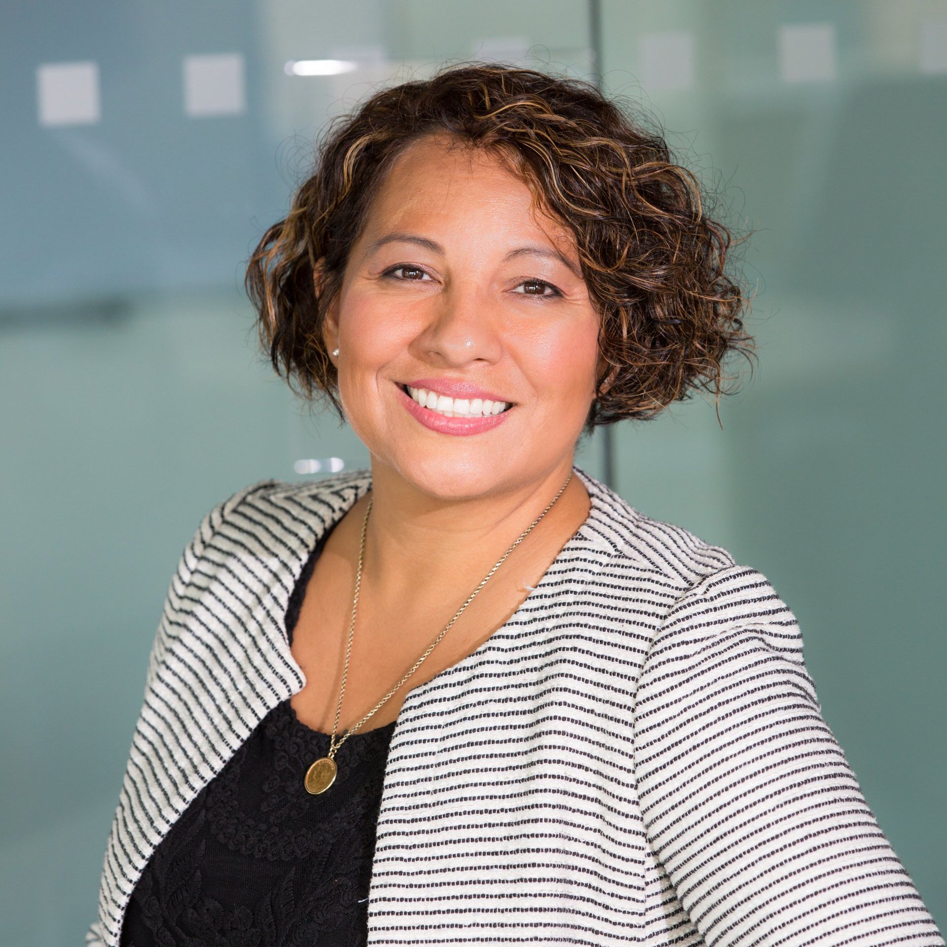 A woman wearing a striped jacket and a necklace is smiling for the camera.