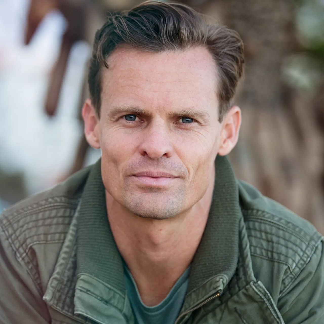 A man in a green jacket is looking at the camera