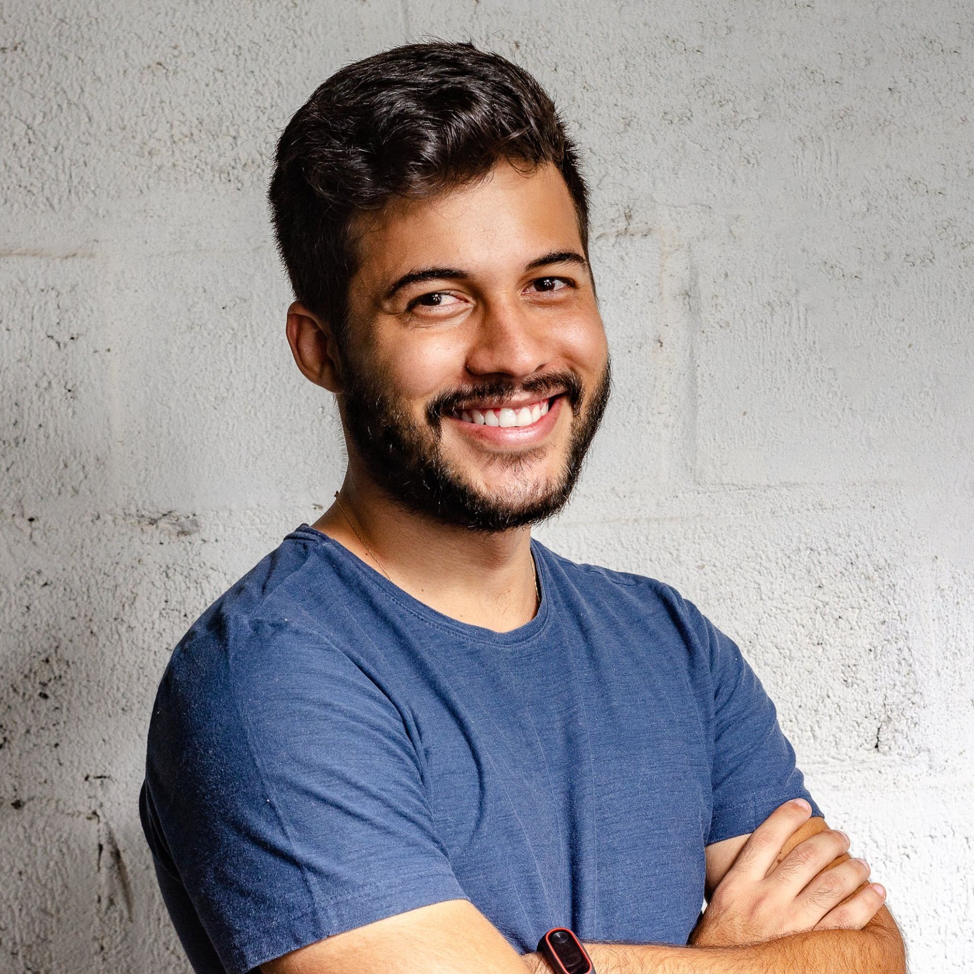 A man with a beard is wearing a blue shirt and smiling with his arms crossed.