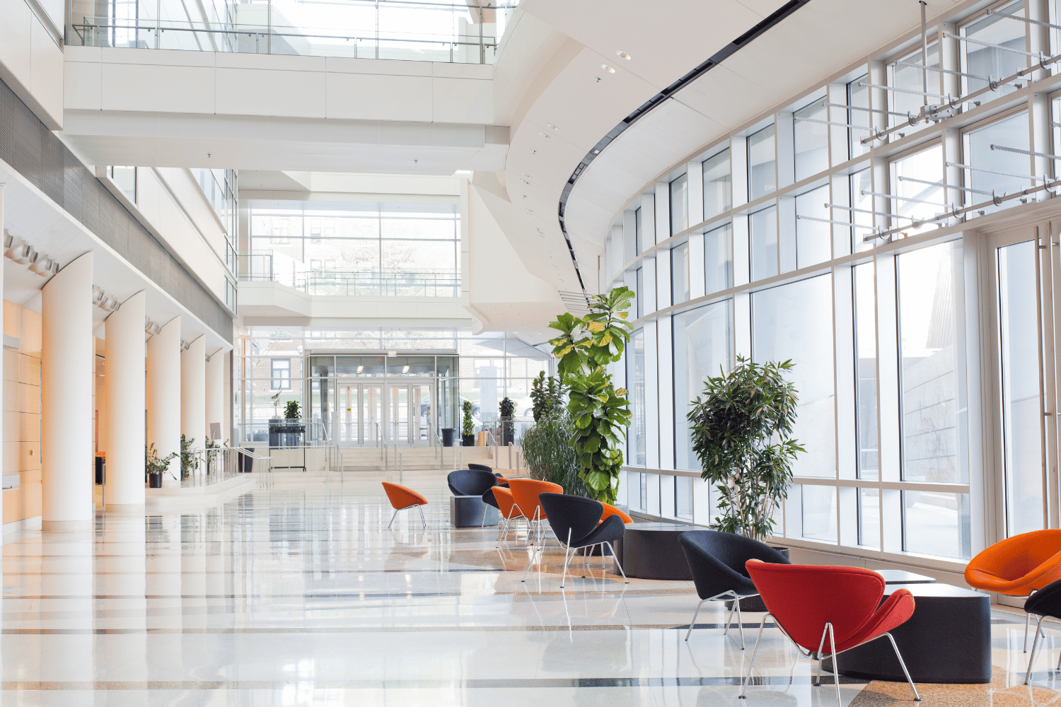 A long hallway in a building with lots of windows and chairs.