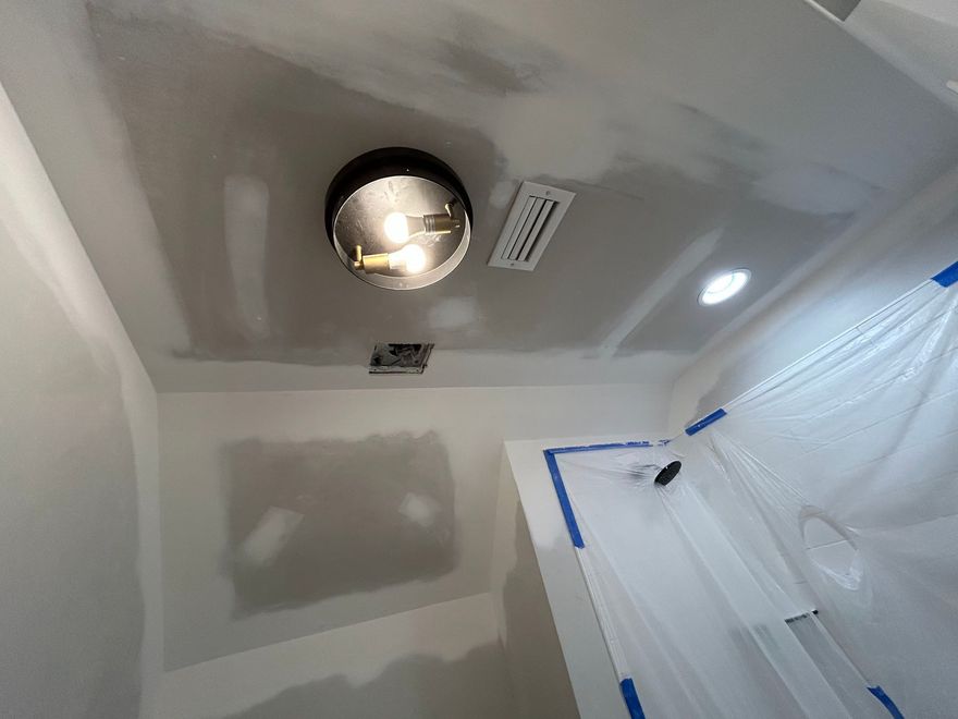 Bathroom ceiling with recessed light, vent, and blue tape over plastic-covered walls during renovation