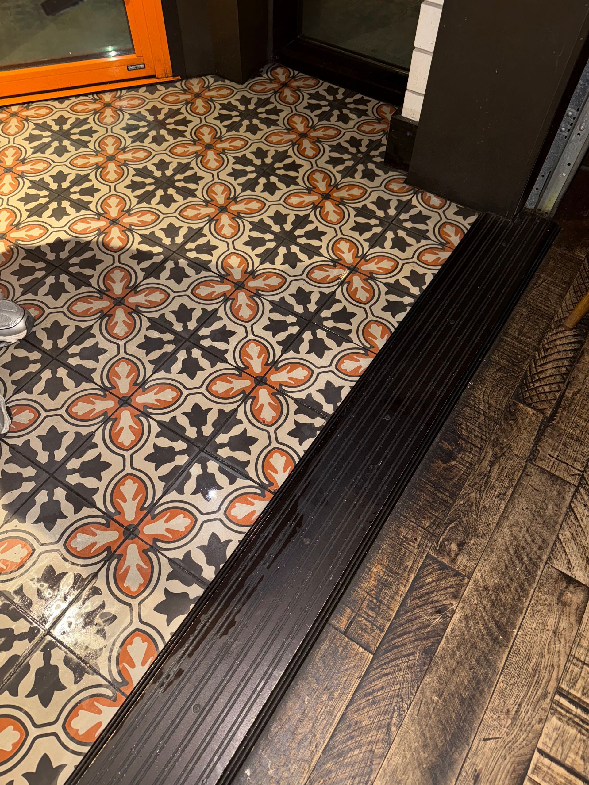 Ornate tile floor meets dark wooden floor with a textured black threshold.