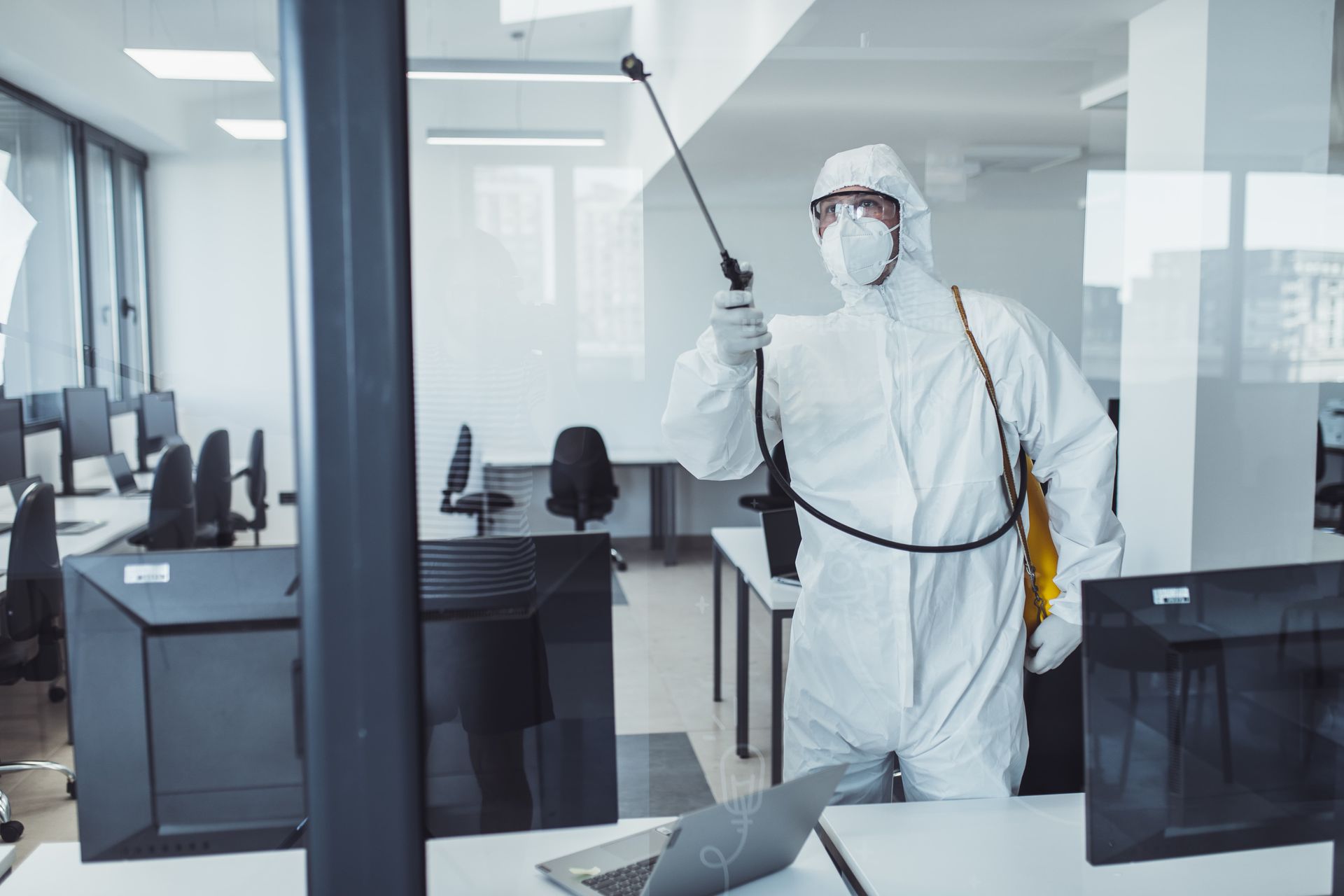 Person in protective suit sanitizing an office with a sprayer.