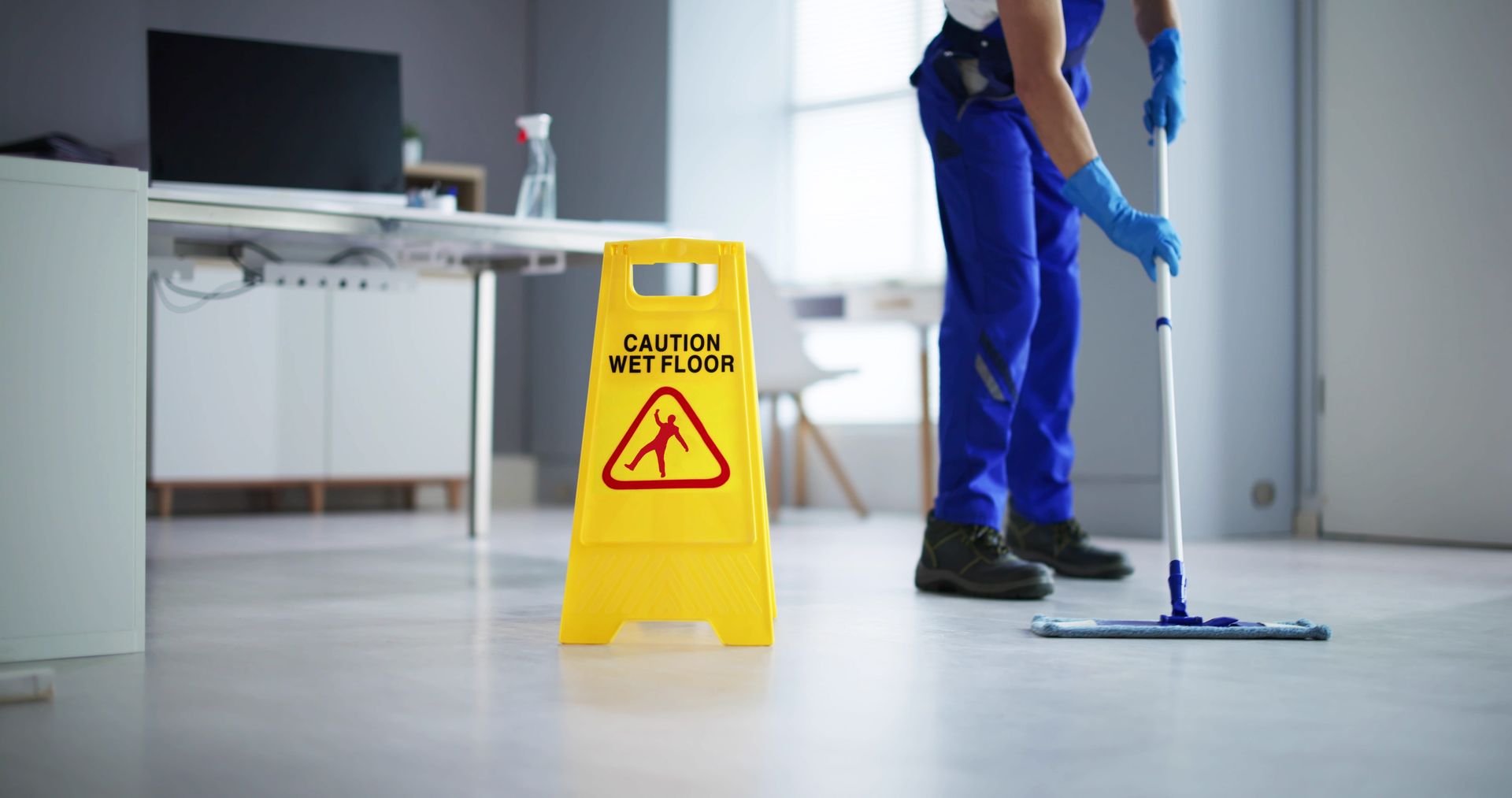 Janitor mopping a floor, yellow caution sign in the foreground.