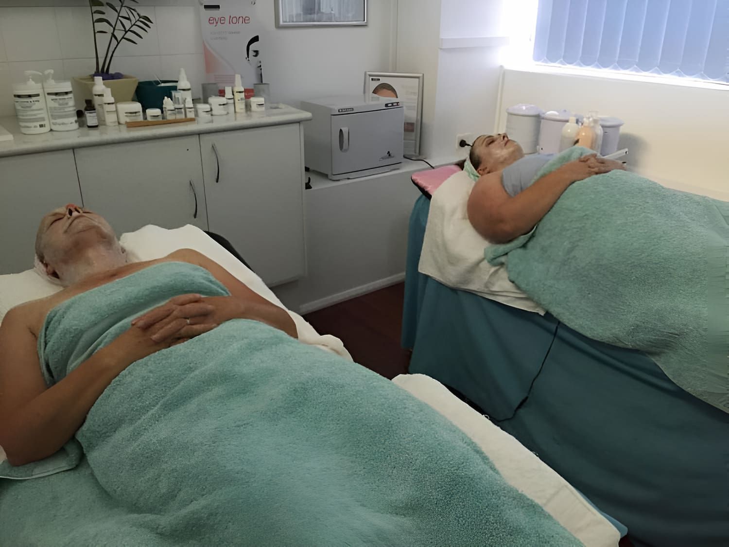 Two Women Wrapped In Blue Towels Are Laying On Massage Beds — InHarmony Skin & Beauty Clinic In The Entrance, NSW