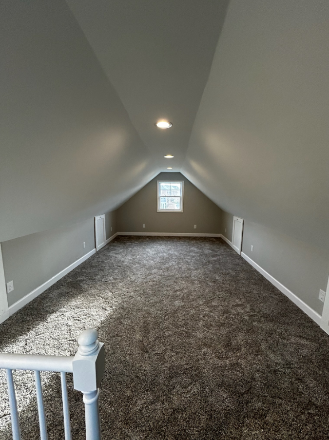 An empty attic with a staircase and a window.