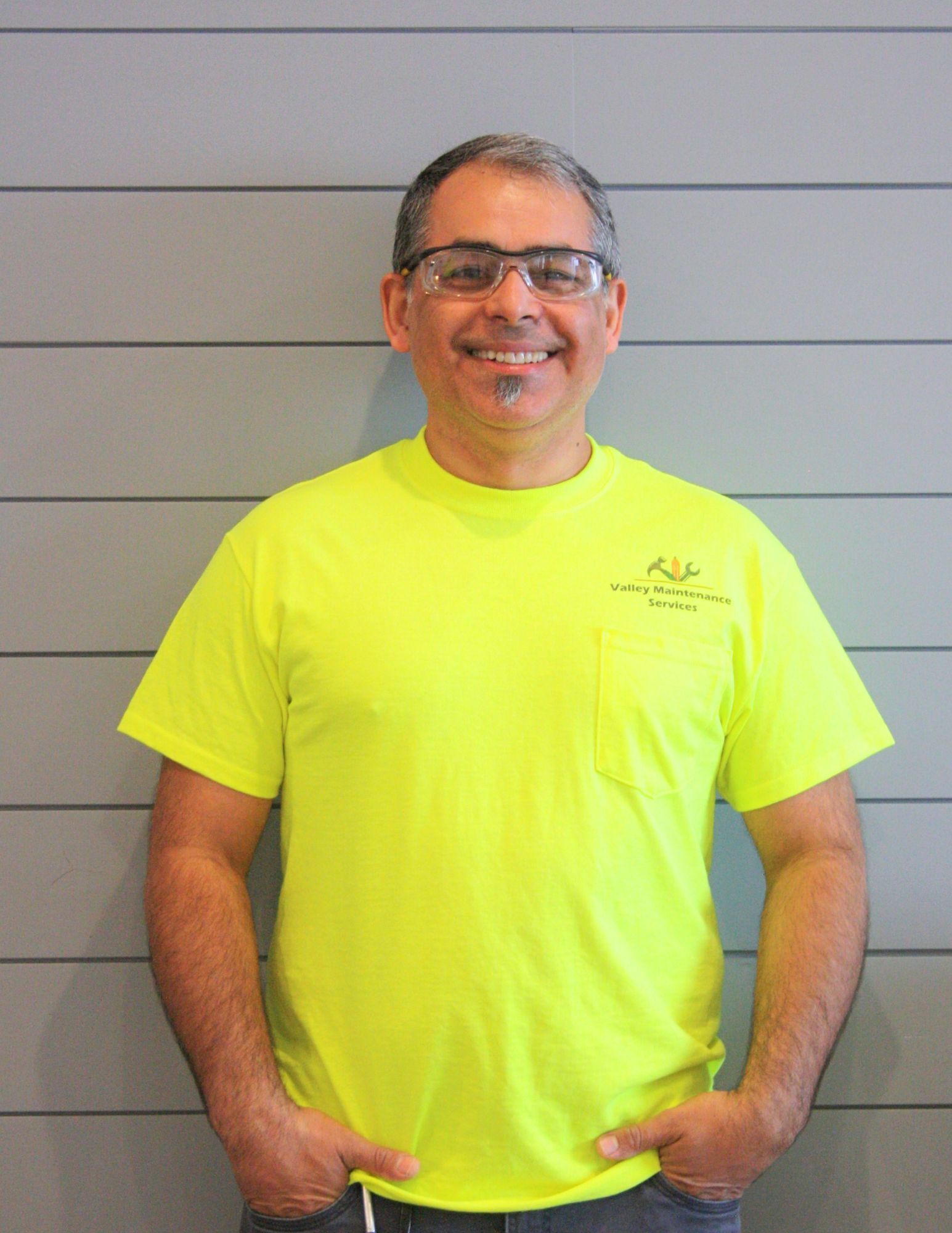 A man wearing a neon yellow t-shirt and glasses is standing with his hands in his pockets.