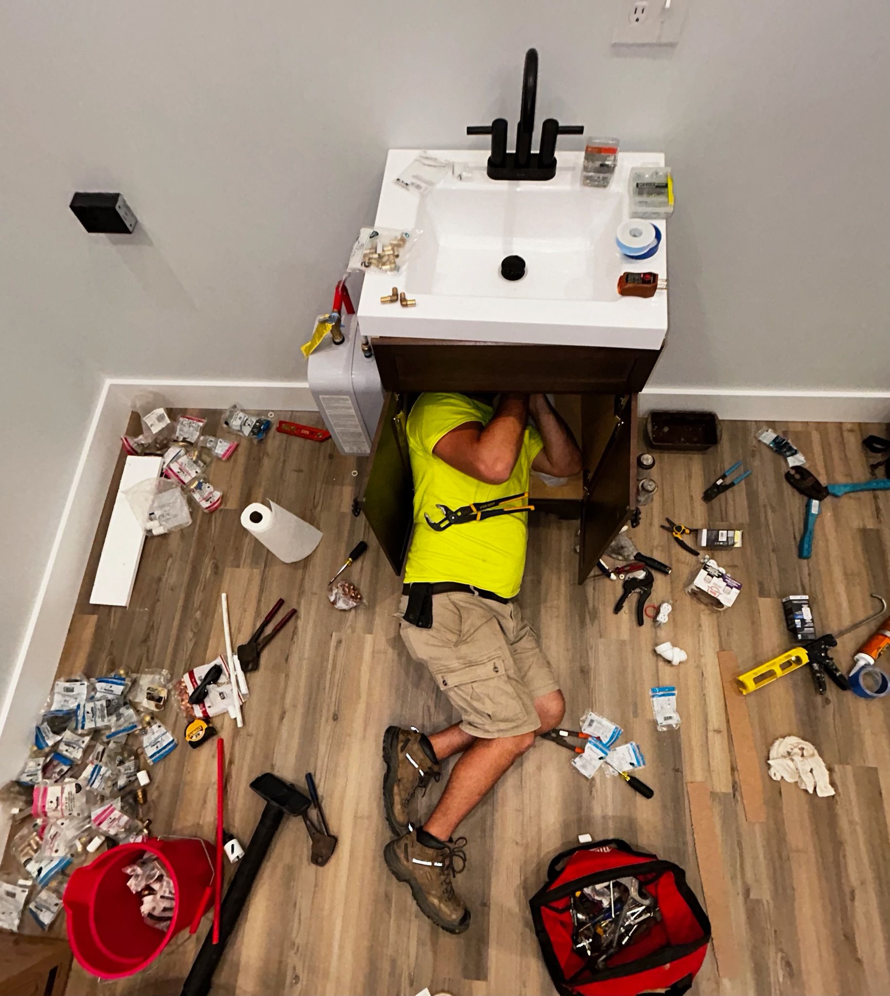 A man is laying on the floor under a sink.