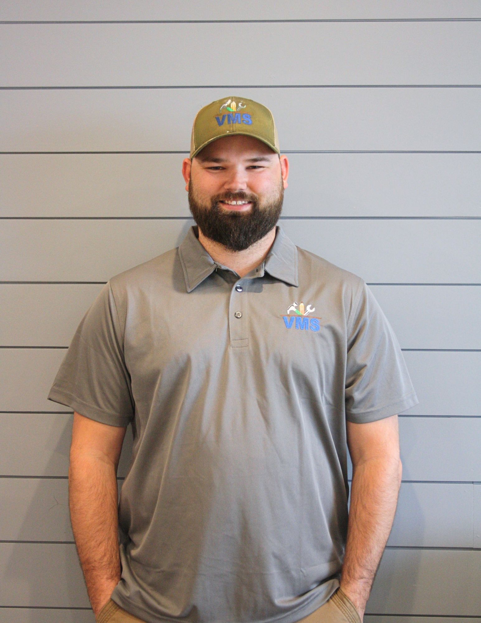 A man with a beard is wearing a polo shirt and a hat.