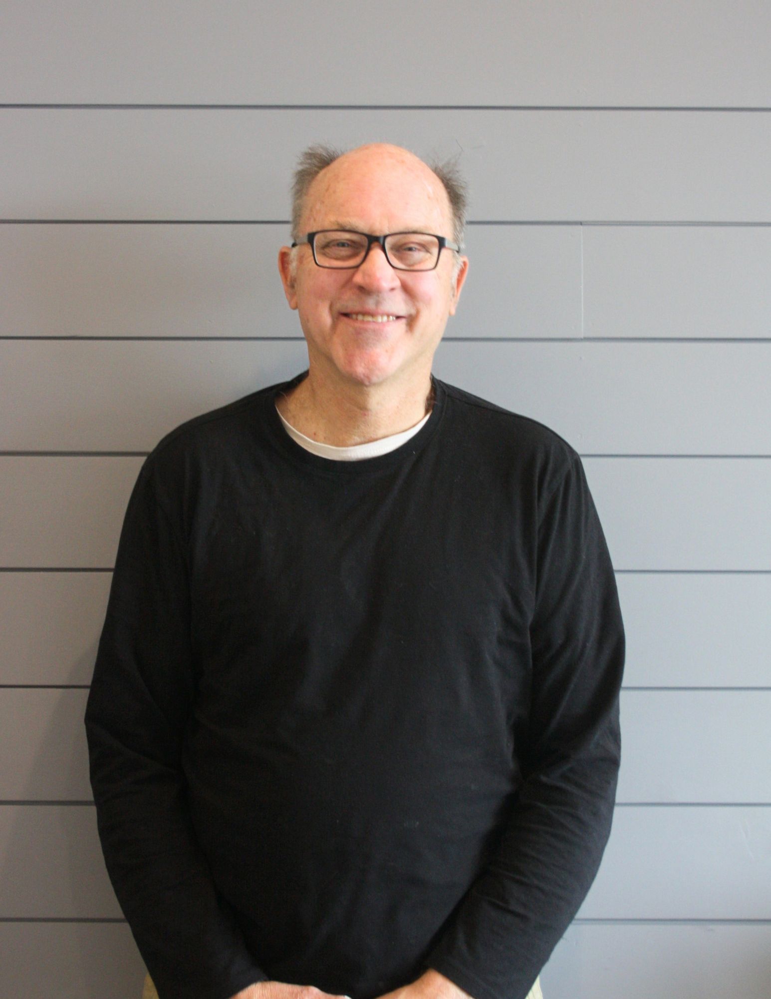 A bald man wearing glasses and a black shirt is smiling for the camera.