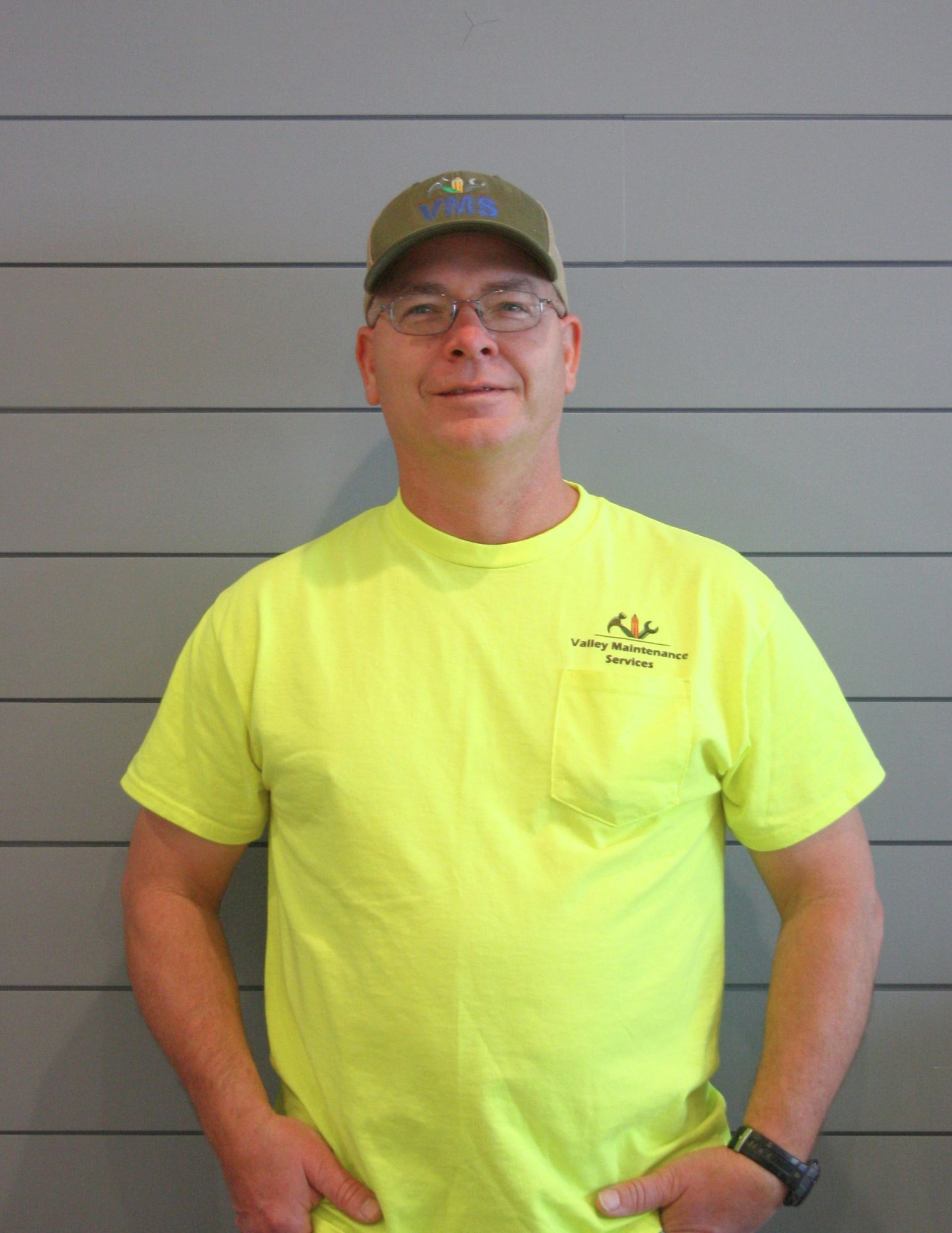 A man wearing a yellow shirt and hat is standing with his hands in his pockets.