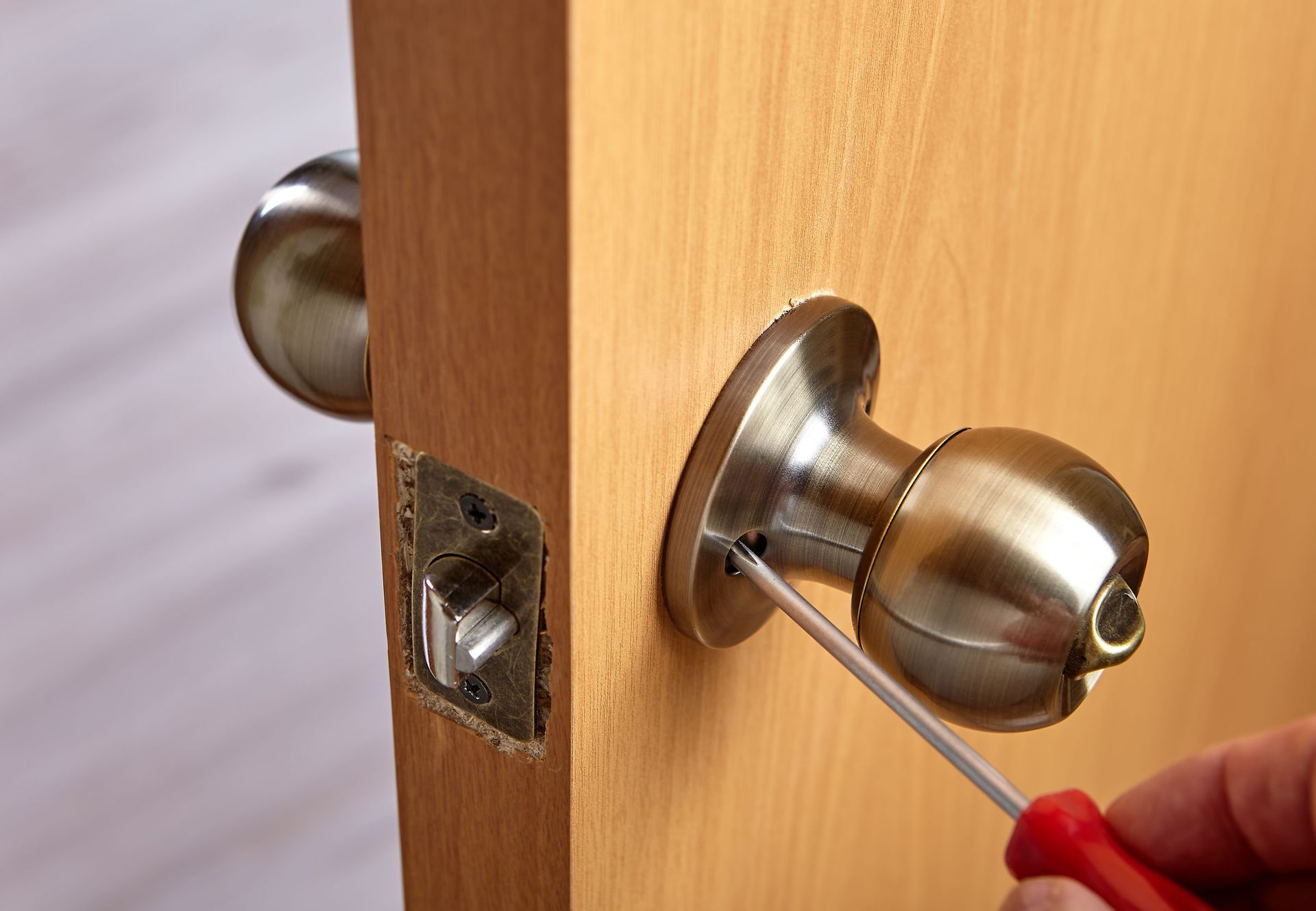 A person is fixing a door knob with a screwdriver.