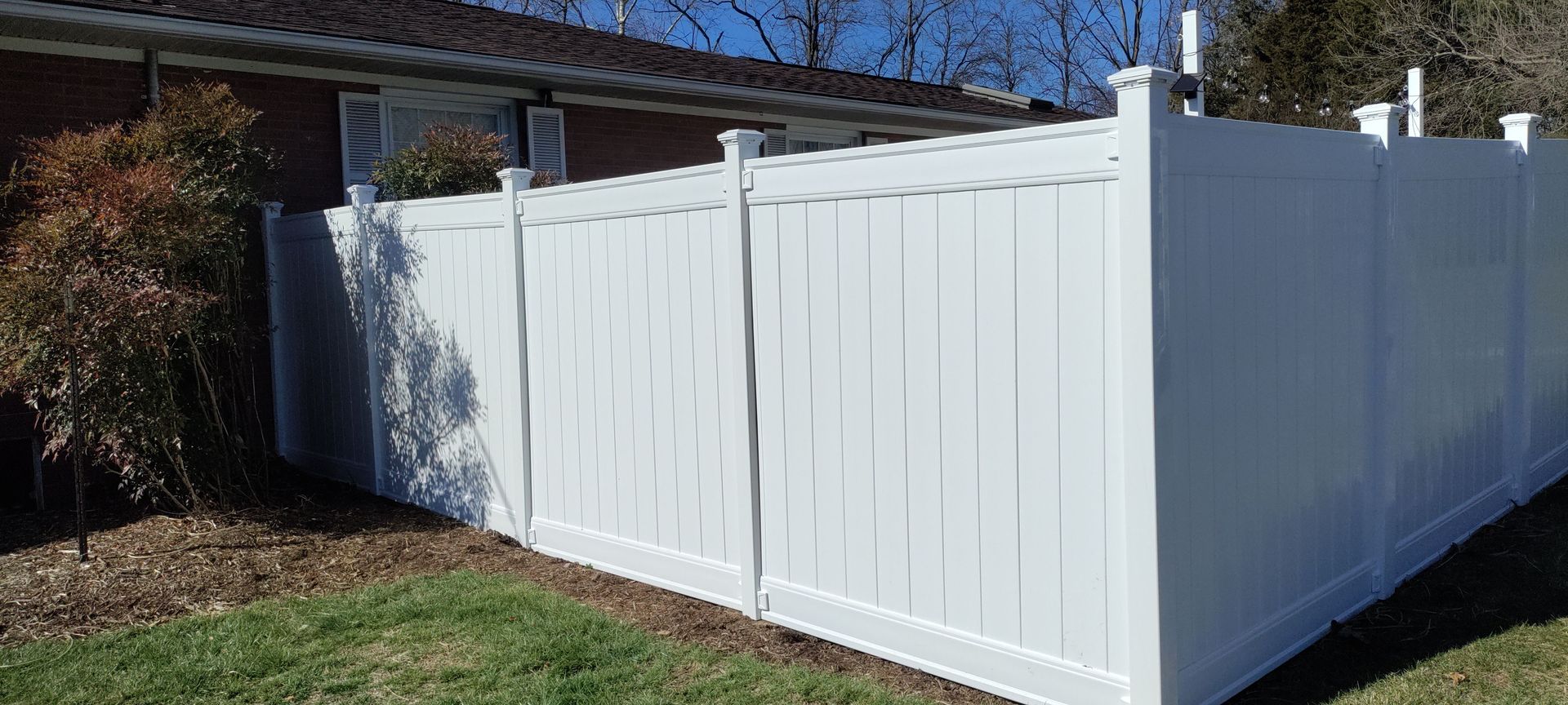 A white vinyl fence is sitting in the grass in front of a house.