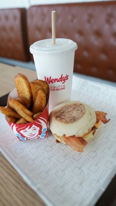 Wendy's breakfast meal: Egg and bacon sandwich, potato wedges, and a drink with a straw, all on a tray.