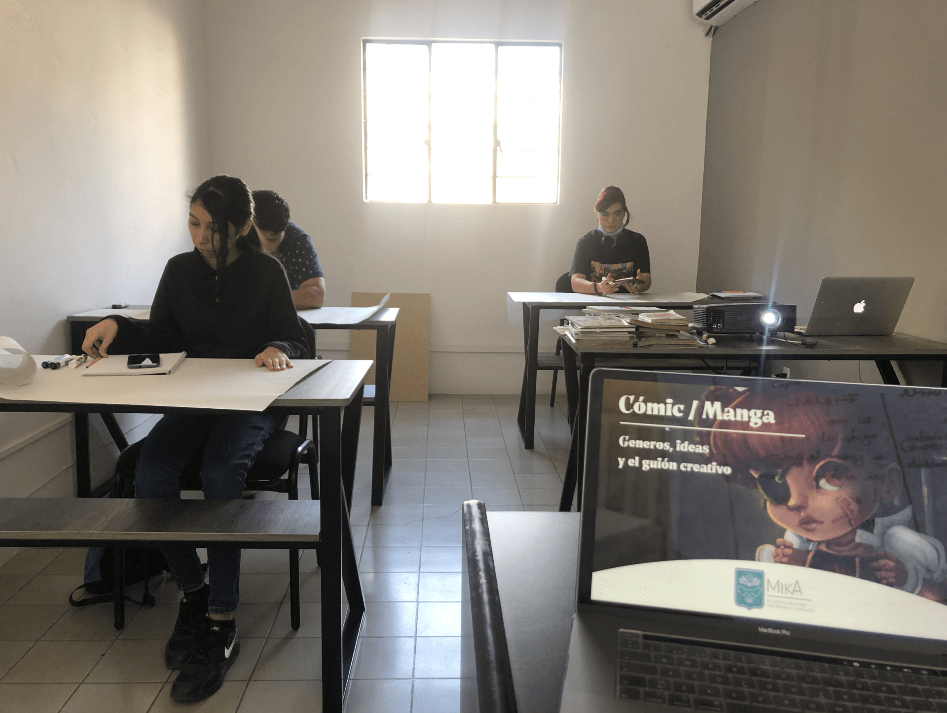 Un grupo de personas están sentadas en escritorios en un aula.