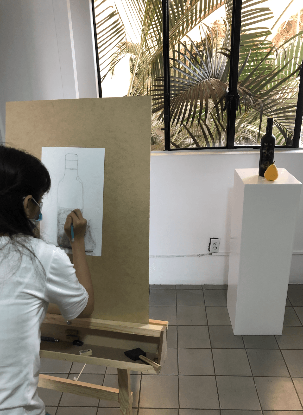 Una mujer está dibujando una botella en un caballete.