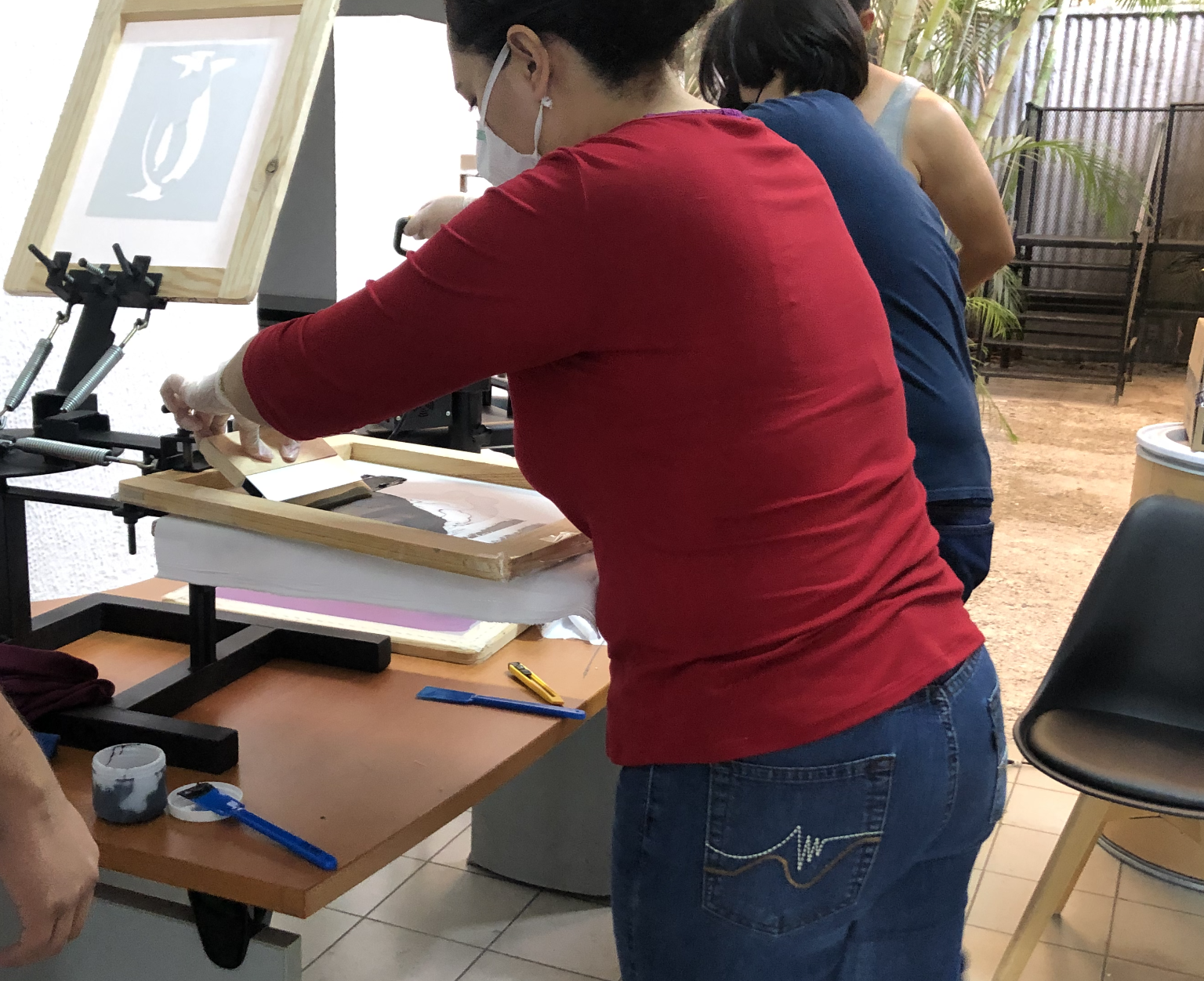Una mujer con una camisa roja está trabajando en una máquina de serigrafía.