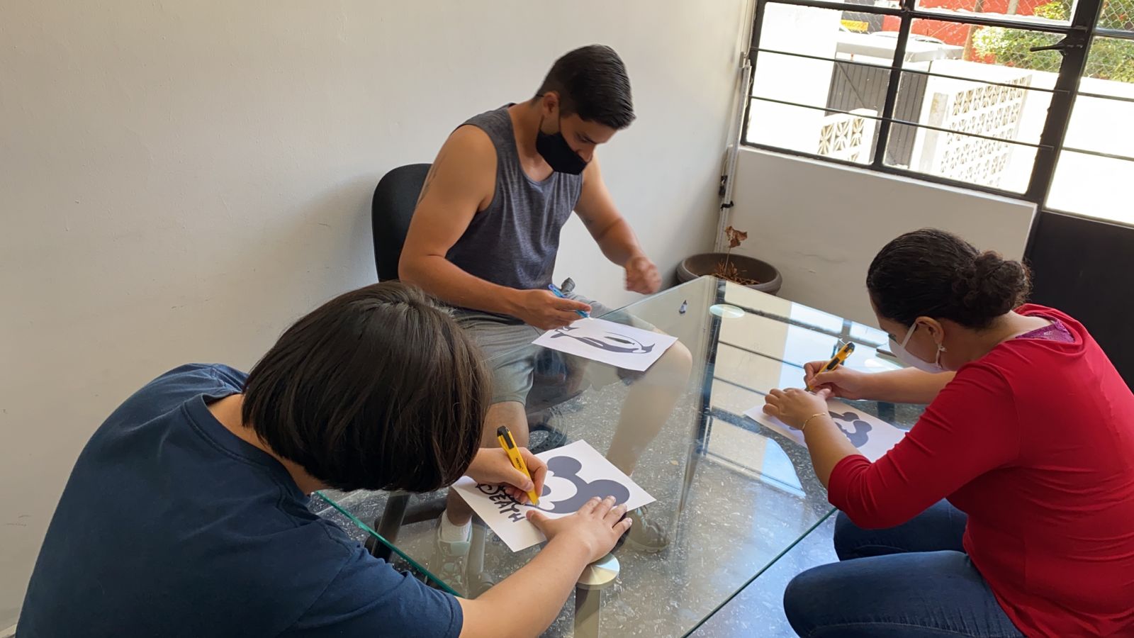 Un grupo de personas están sentadas alrededor de una mesa dibujando en papel.