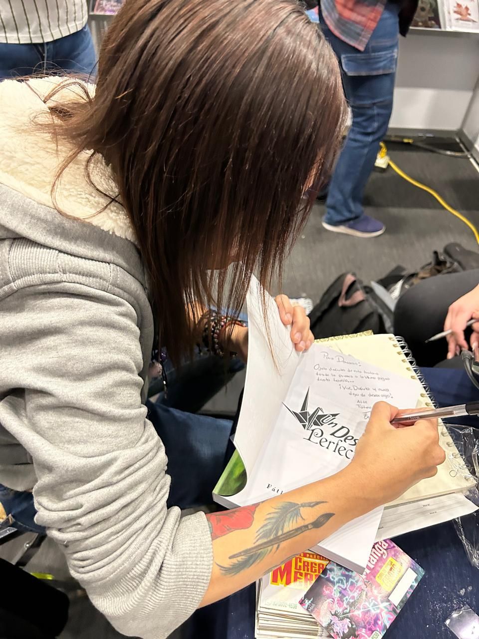 Una mujer con un tatuaje en el brazo está firmando un libro.