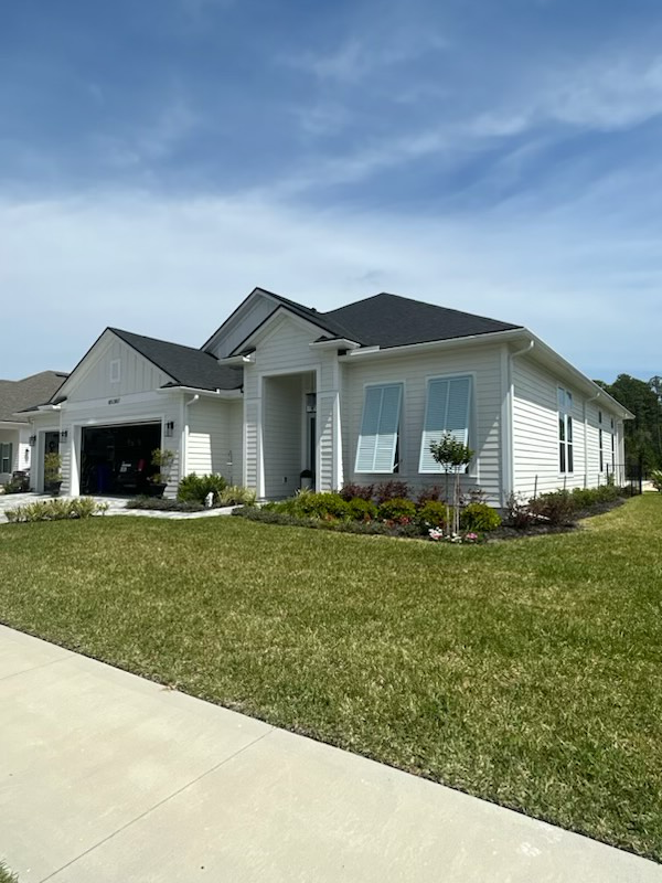 a white house with a black roof is sitting on top of a lush green lawn