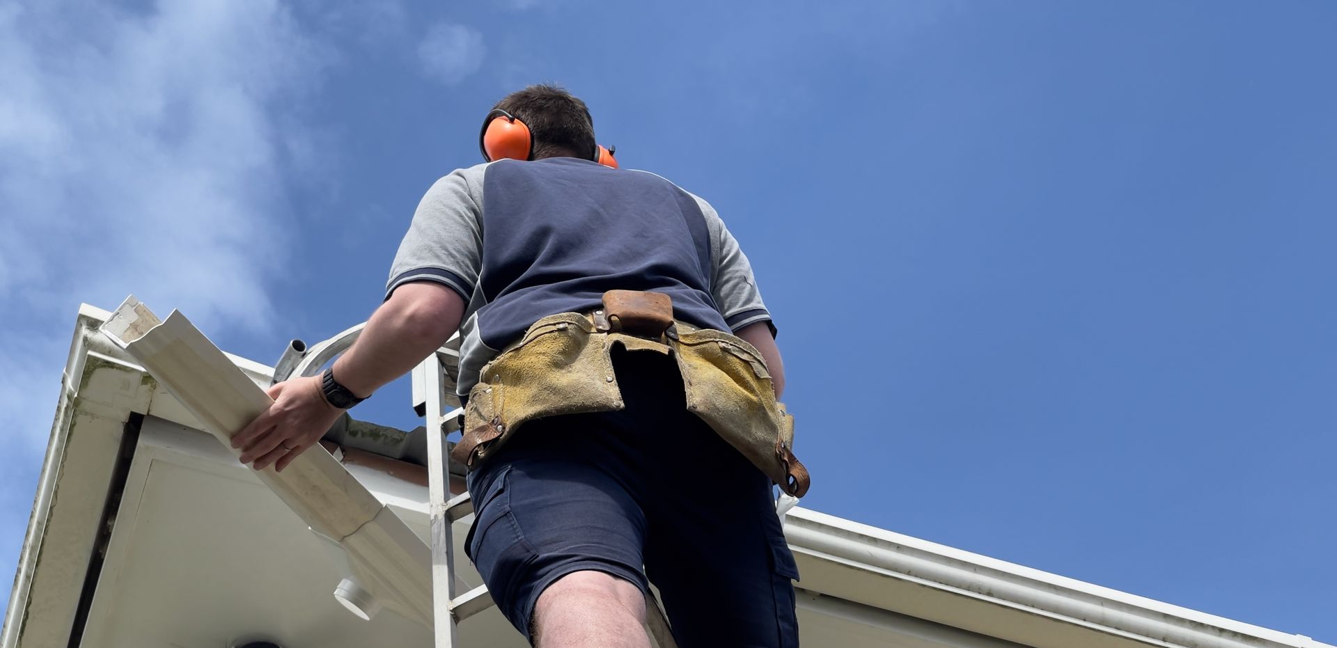 a man is standing on a ladder on top of a house holding a gutter