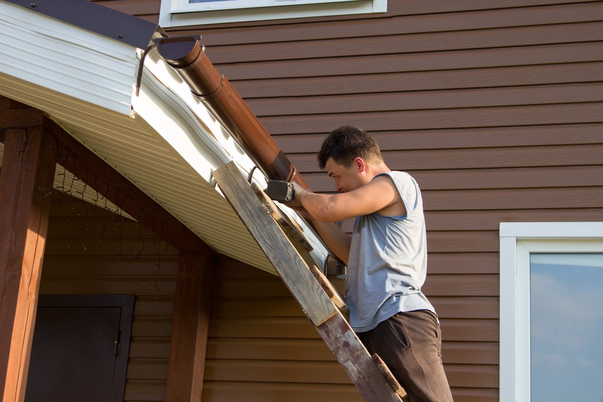 a man is standing on a ladder fixing a gutter on the side of a house