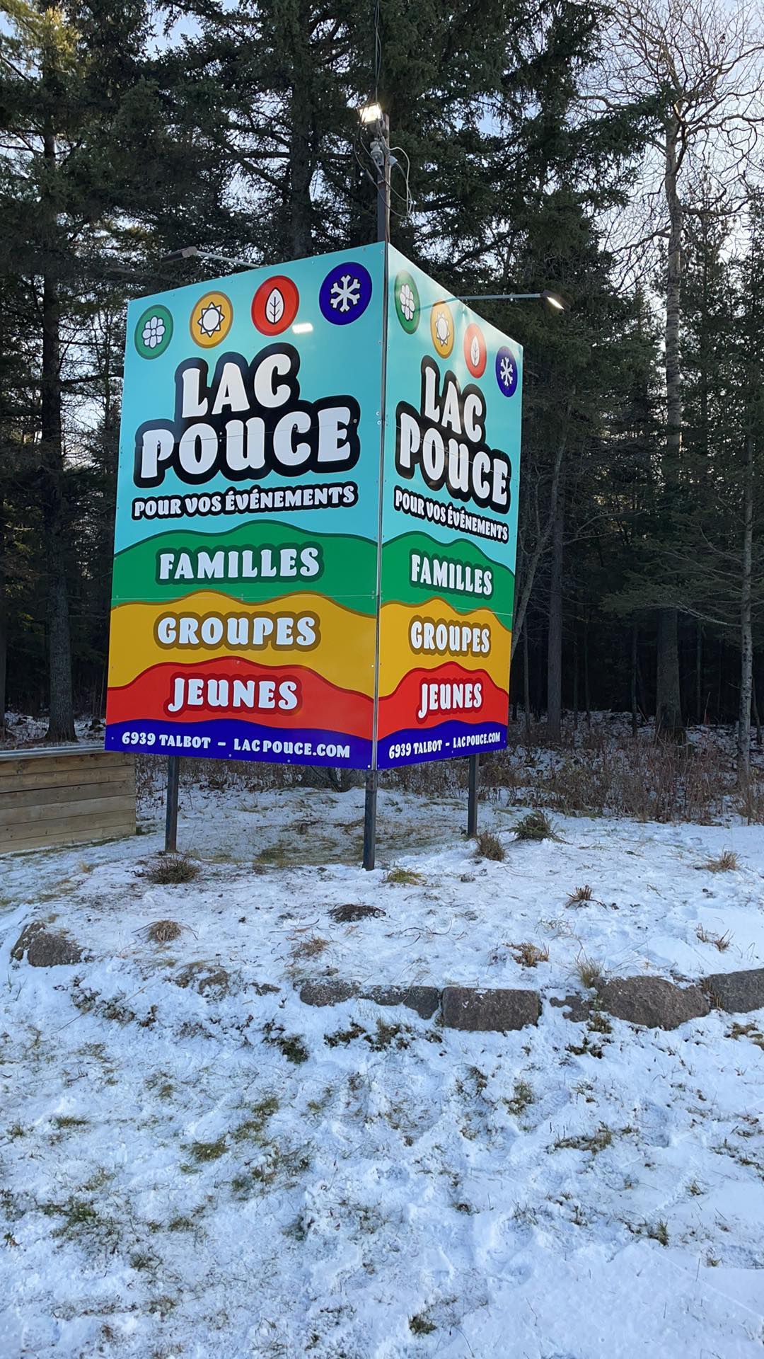 Un panneau coloré est posé dans la neige devant une forêt.