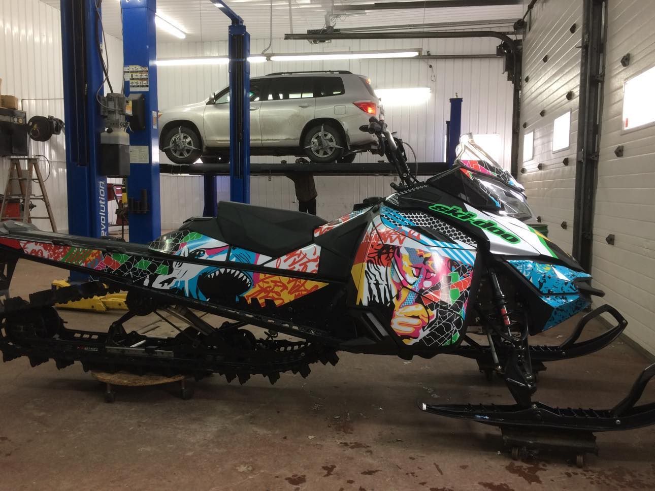 Une motoneige est garée dans un garage avec une voiture en arrière-plan.