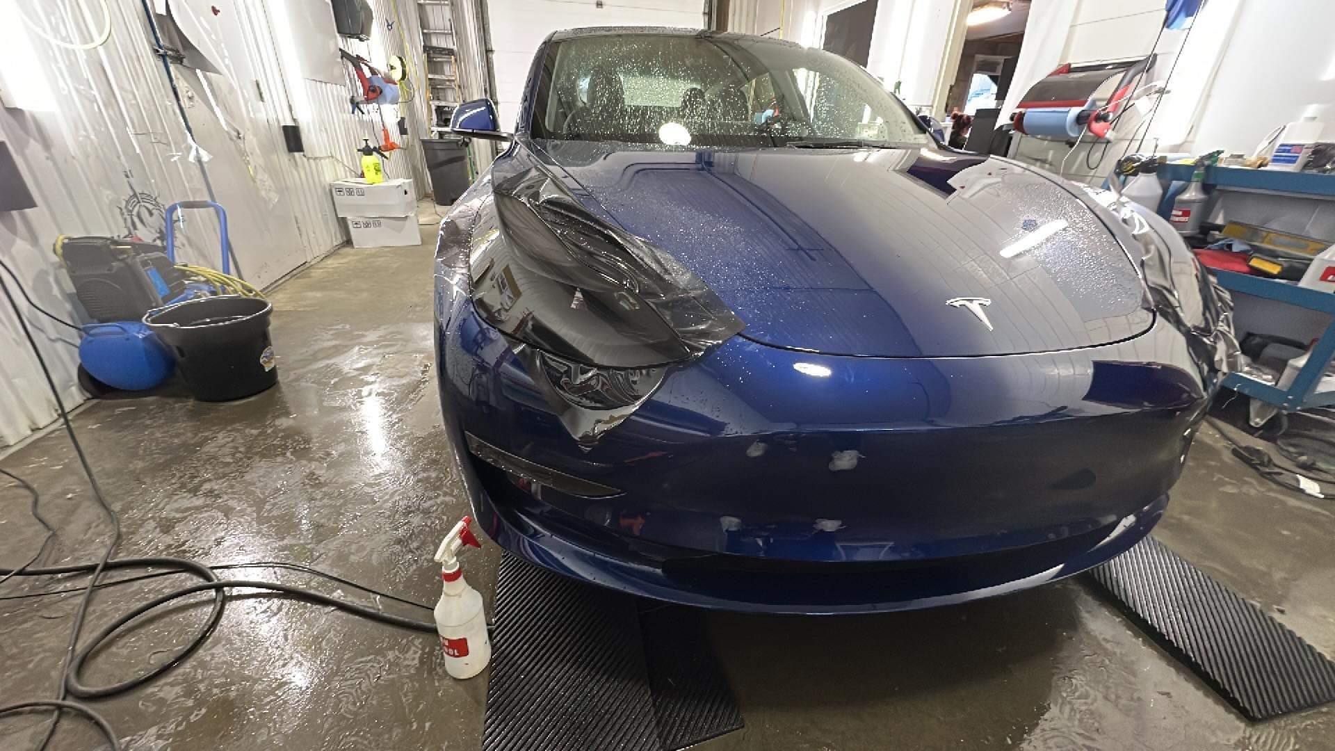 Une Tesla Model 3 bleue est enveloppée dans du plastique dans un garage.